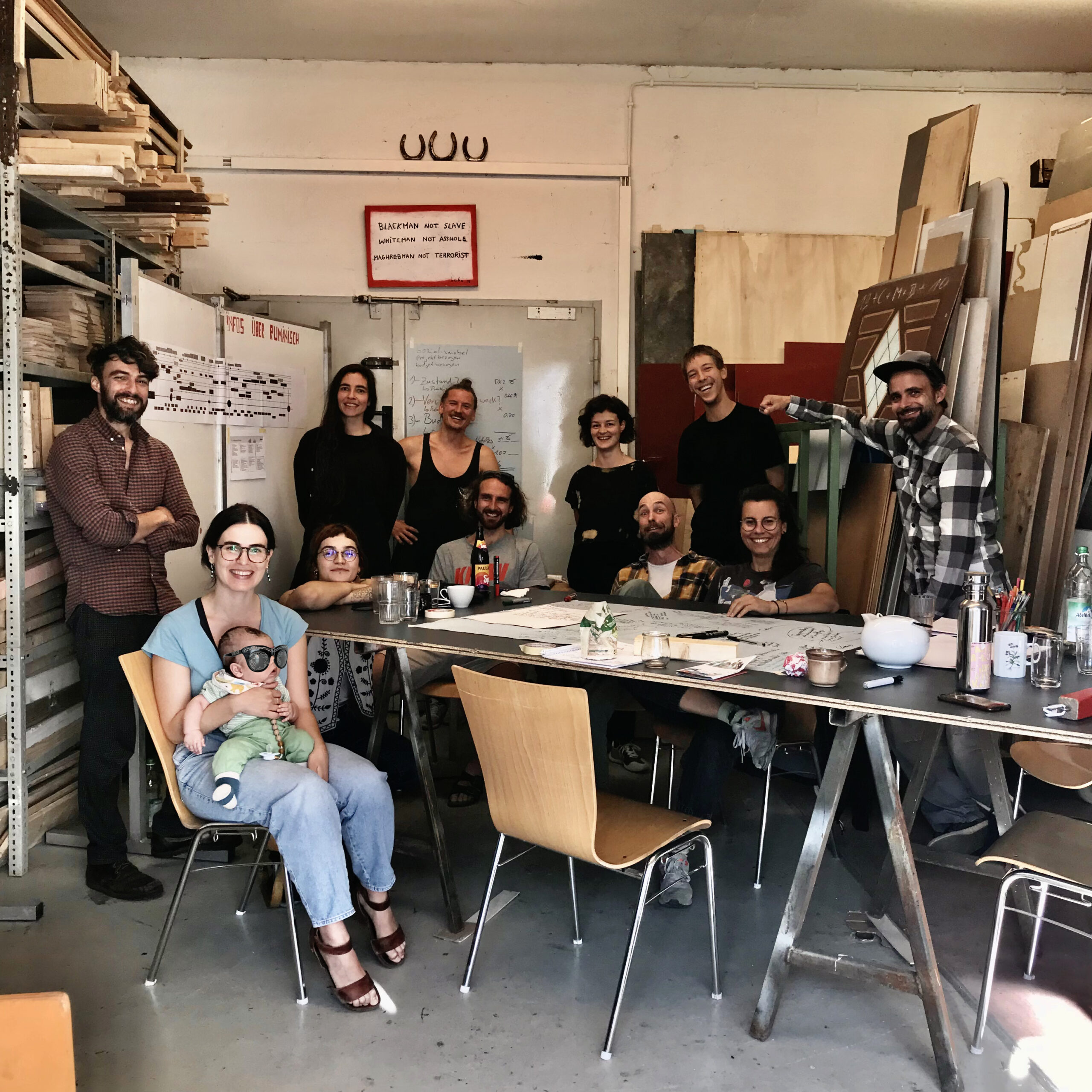 Das treibgut Team im eigenen Materiallager an einem großen Schreibtisch. Alle Teammitglieder blicken offen und lächelnd in die Kamera.