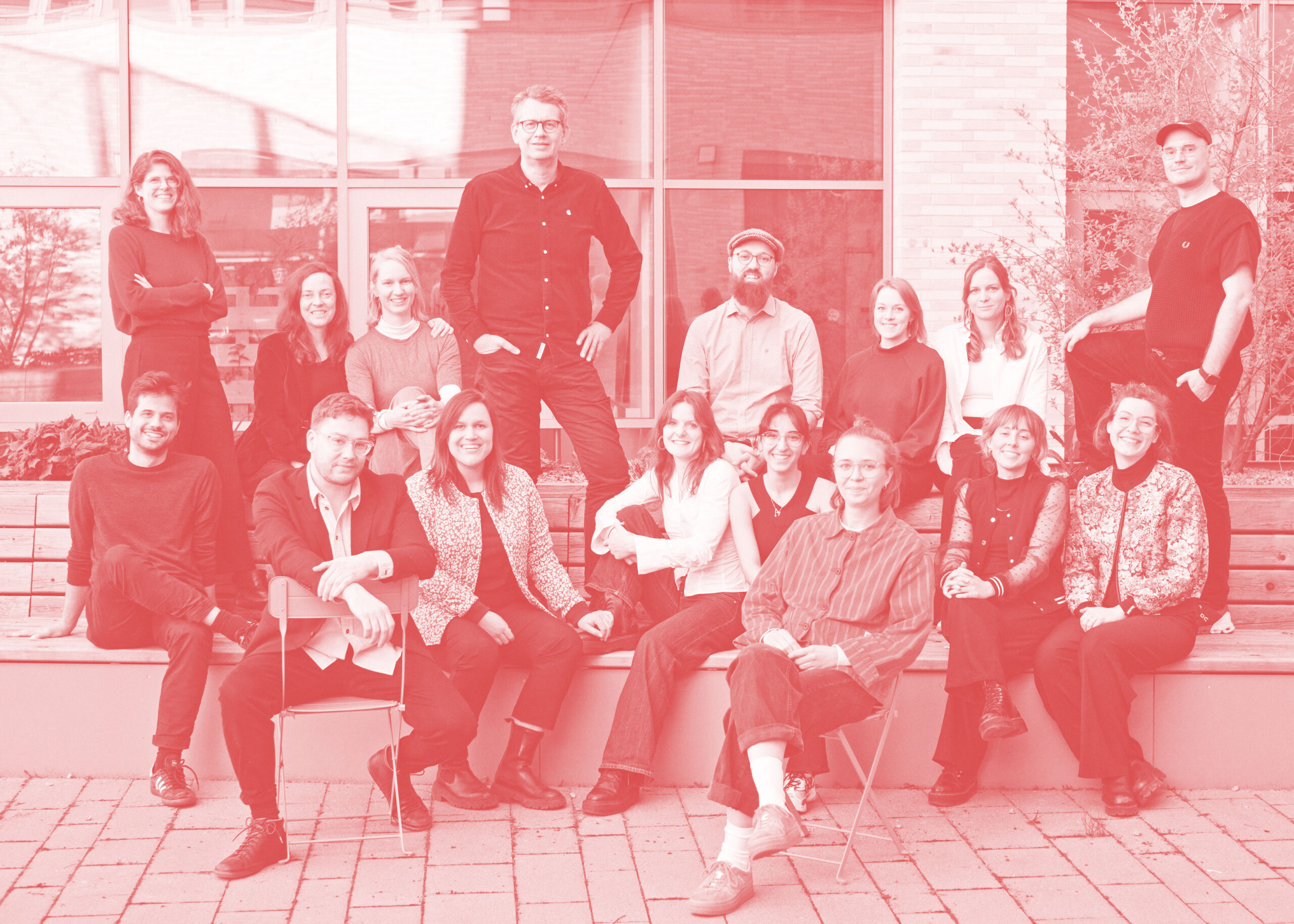 Teamfoto-2025 Gruppenfoto des social design lab Team, in einem Innenhof, teils sitzend teils stehend. Auf dem Foto liegt ein roter Filter