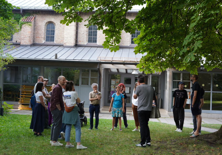 Mehrere Menschen stehen in einer Gruppe im Kreis vor einer Kirche und führen ein Gespräch.