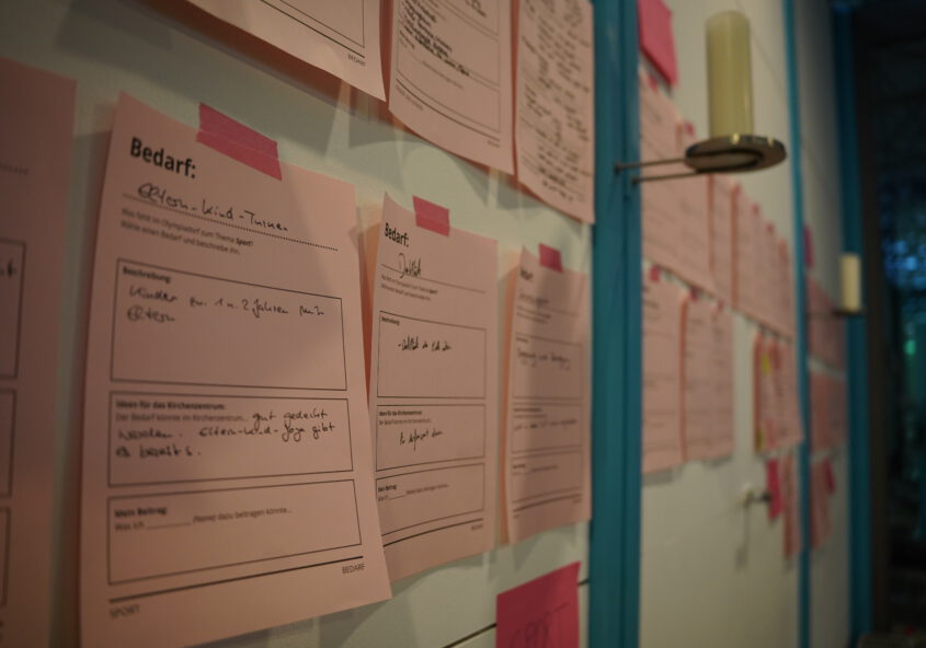 Viele beschriftete Zettel kleben an einer Wand. Sie sind alle mit rotem Tape fixisiert.