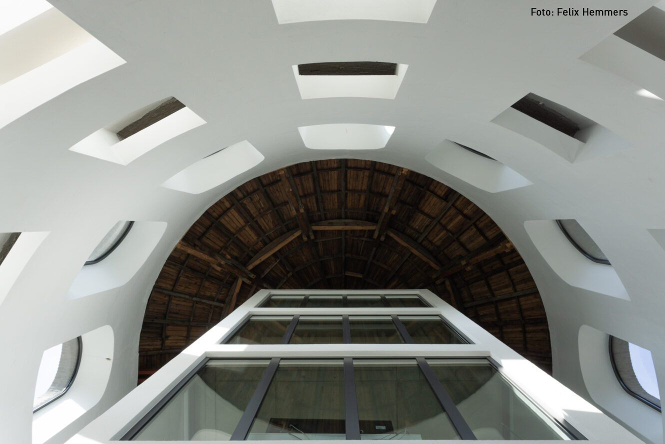 Dreifaltigkeitskirche Münster Blick von unten auf die weiße Innenwand mit rechteckigen Öffnungen und eine gewölbte Holzdecke der Dreifaltigkeitskirche Münster
